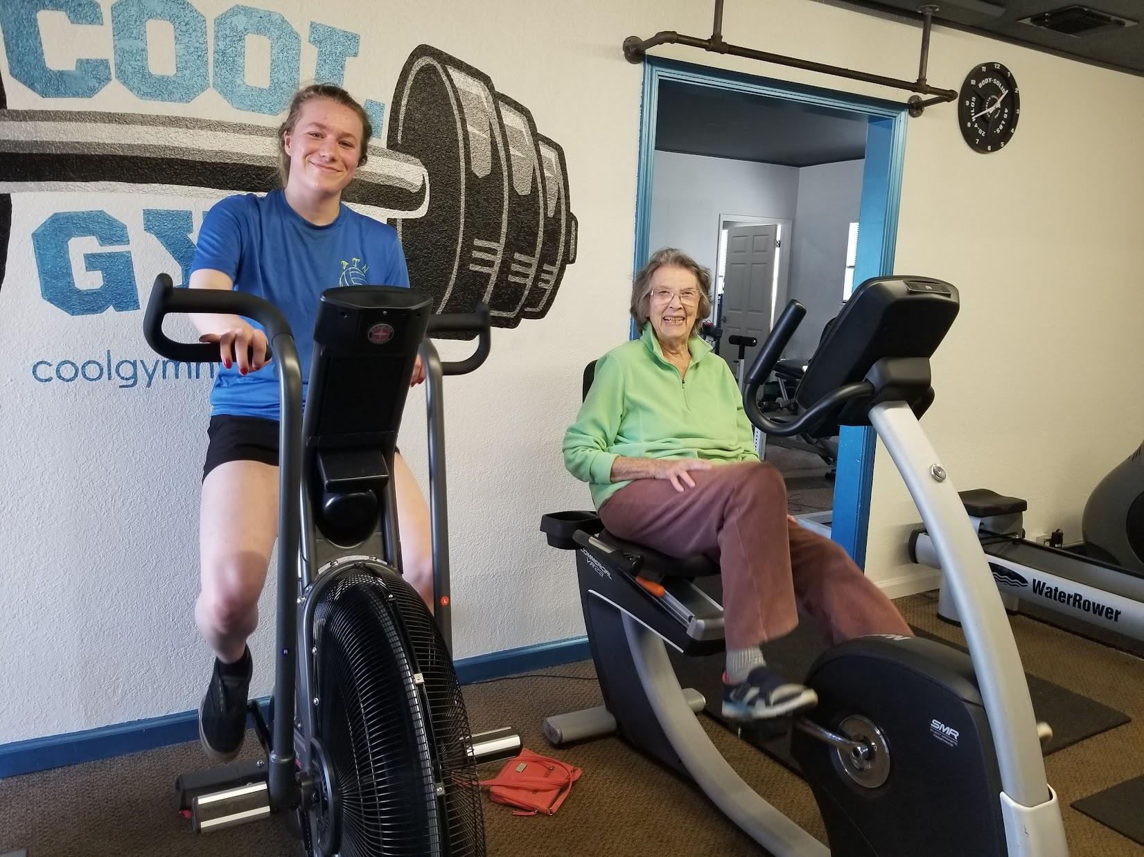 An image of a woman in a blue shirt on an exercise bike and a woman next to her in a green sweater on an bike.